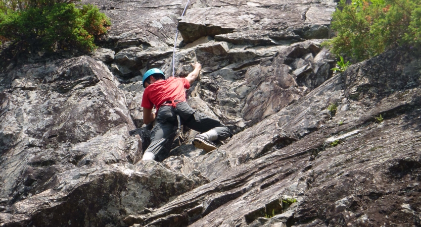 A person wearing safety gear and secured by ropes climbs a rock wall. 